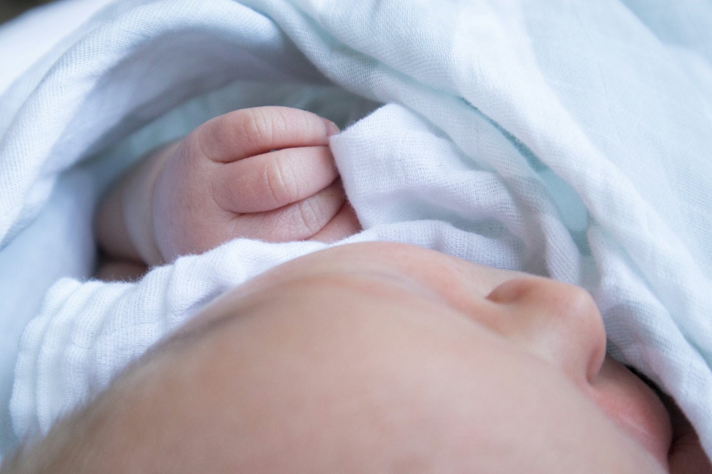 Un neonato avvolto in coperte bianche e blu.
