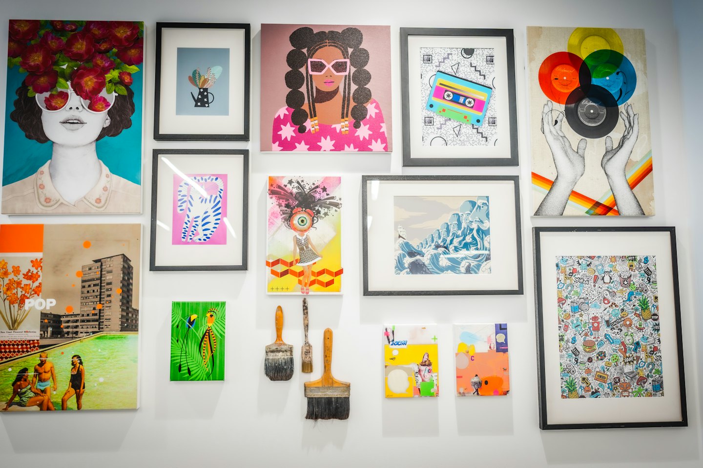 Collezione eclettica di opere d'arte contemporanea e pennelli su una parete di galleria.