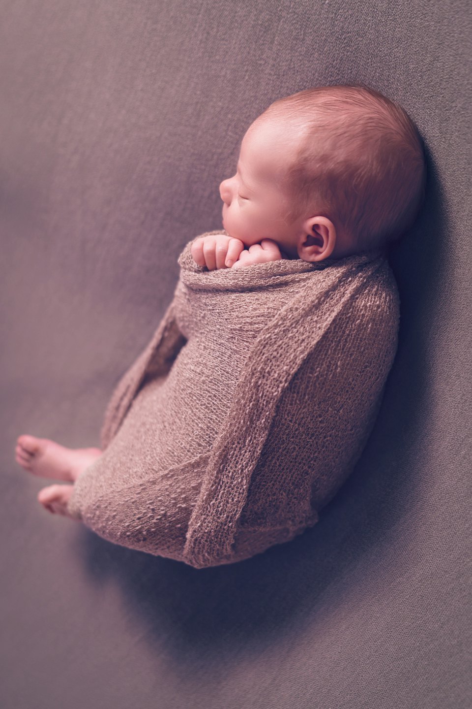 Un neonato dorme avvolto in una coperta marrone lavorata a maglia.
